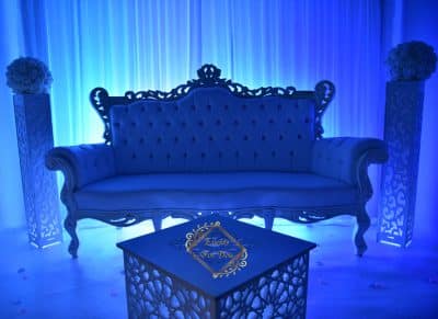 Somptueux canapé baroque blanc, éclairage bleu intense. Décoration de mariage avec colonnes fleuries et table basse gravée portant le logo "Events For You".