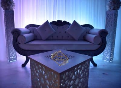 Canapé de luxe blanc sculpté et table marocaine lumineuse pour un salon événementiel. Éclairage violet-bleu intense. Logo Events Saroum.