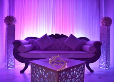 Canapé lounge événementiel violet, avec ambiance lumineuse magenta. Colonnes et table décoratives ajourées. Logo "Lights For You".