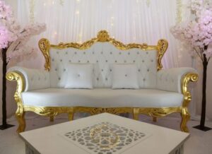 Luxueux canapé royal blanc capitonné et doré pour mariage, encadré par des arbres sakura roses et un décor de rideaux lumineux.