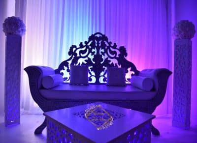 Canapé lounge violet luxe pour mariage et événementiel Magnifique canapé sculpté pour décoration lounge d'événement, éclairé par des lumières bleues et violettes. Piliers floraux. Logo "Events For You".