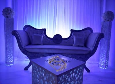 Sofa de luxe oriental et table basse illuminée pour événementiel. Décoration chic sous lumière bleue avec piliers floraux.