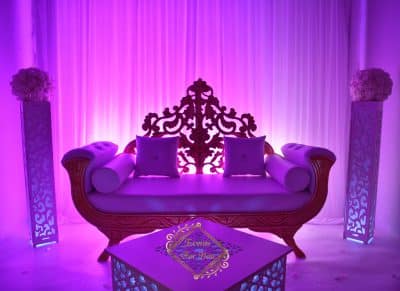 Scène de mariage romantique: trône royal pourpre, colonnes lumineuses et tentures blanches. Table basse affichant "Excellence For Your Day".