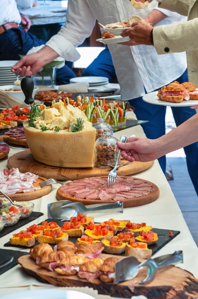 Buffet apéritif italien : fromages, charcuterie gourmet. Buffet italien gourmet : meule de Parmesan, charcuterie, bruschetta, et crudités. Des invités se servent lors d'un élégant apéritif dînatoire.