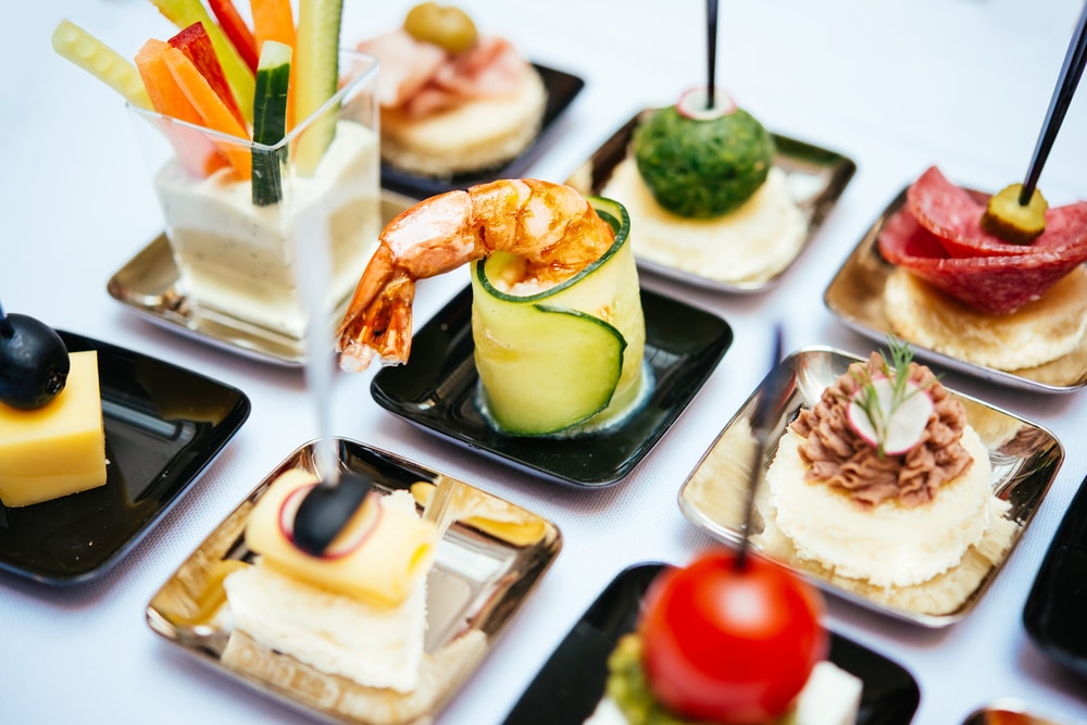 Buffet de mariage somptueux sous les lumières Vaste buffet de réception en extérieur : tartes salées, salades, mignardises et assiettes empilées, éclairé par des guirlandes chaudes.