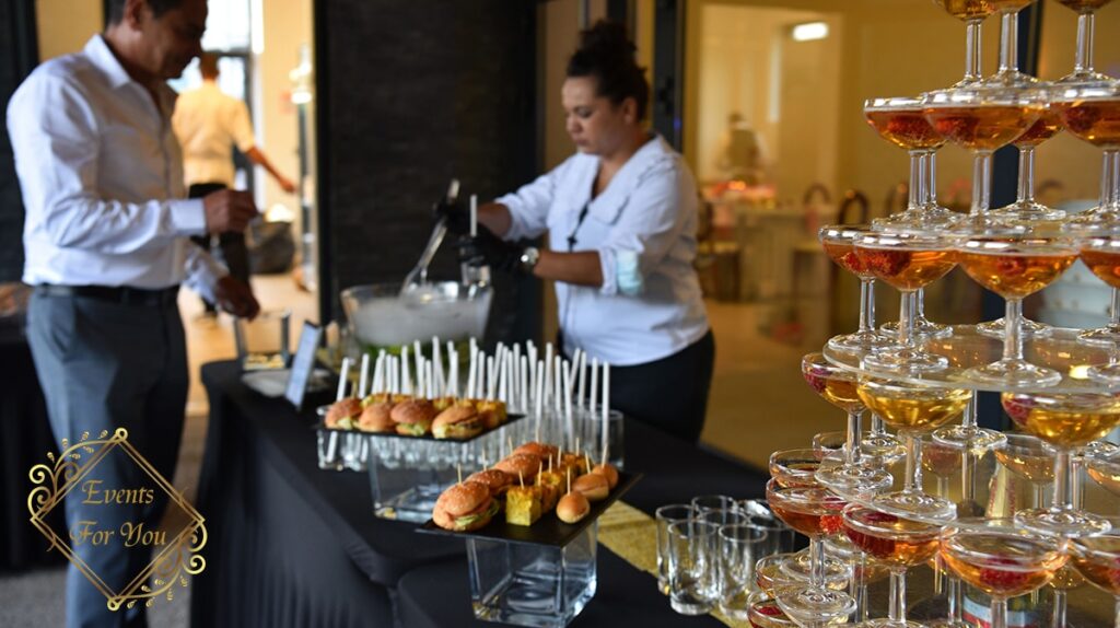 Traiteur événementiel: pyramide de cocktails et buffet. Buffet traiteur Events For You avec serveuse, pyramide de verres cocktails, mini-burgers et verrines. Service élégant.