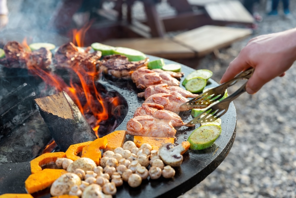 Grillade au brasero : viandes et légumes au feu de bois Cuisson au barbecue de viandes, champignons et courgettes sur un brasero circulaire avec un feu de bois vif.