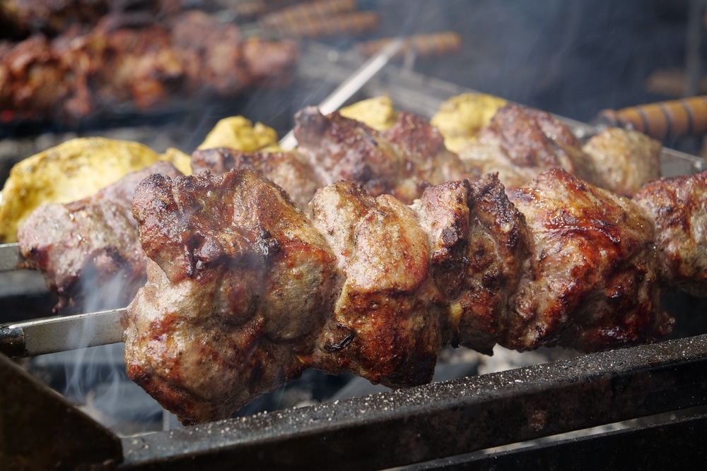 Brochettes de Viande Grillées : Plaisir du Barbecue Brochettes de viande juteuses grillant sur un barbecue avec de la fumée, gros plan de morceaux bien cuits et dorés.